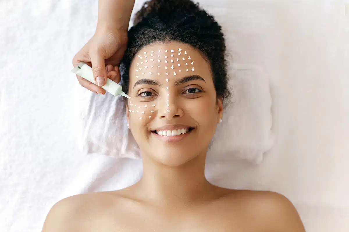 Beauty concept, skincare.Top view of gorgeous hispanic or brazilian woman, with naked shoulders, lying during a skincare procedure with a cosmetologist which applying moisturizing cream on girl's face