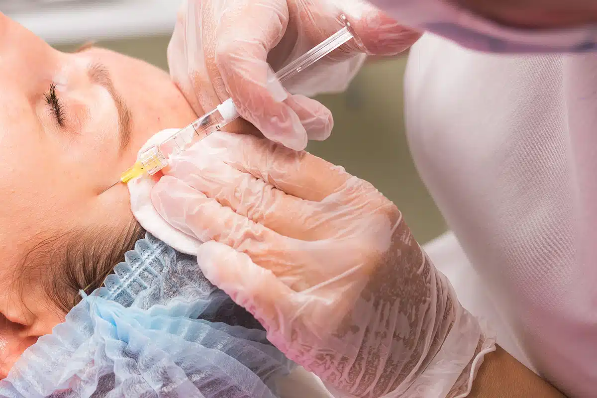 Close up of hands of young cosmetologist injecting in female face